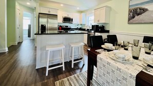 Une cuisine moderne avec des meubles blancs, un îlot central doté de tabourets et un coin repas avec une table dressée pour quatre personnes.