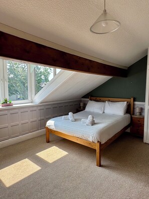 A bedroom with a sloped ceiling, a bed with rolled towels, a bedside table, and a window with a view of trees. - Windermere Cottage for 8 | Walk Everywhere. Authentic Lakeland slate cottage, (Windermere)
