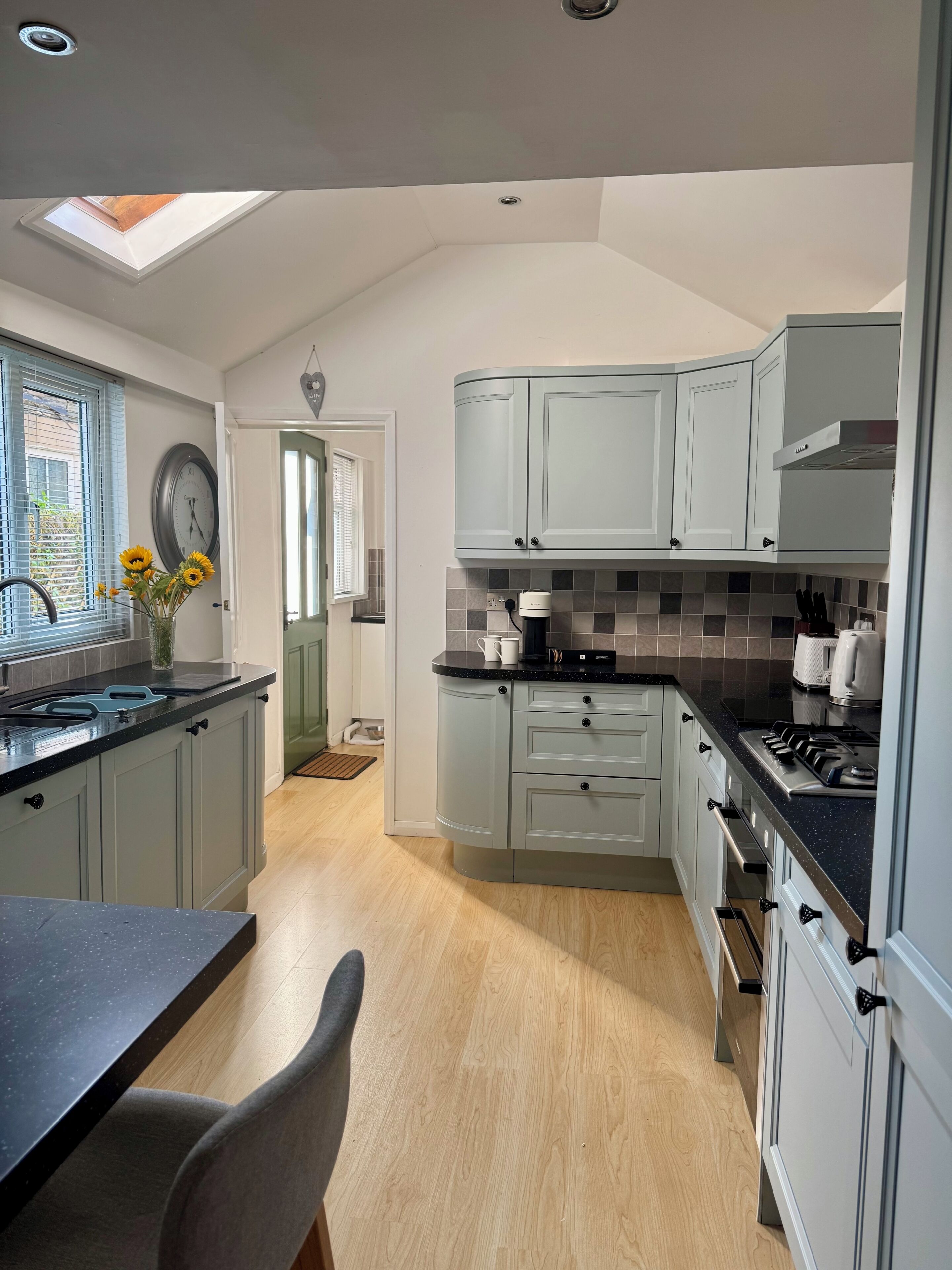 A kitchen with grey cabinets, a black countertop, a built-in oven, and a skylight.