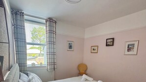 Ein Hotelzimmer mit Bett, Stuhl, kleinem Tisch und einem Fenster mit Vorhängen.