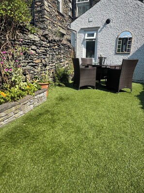 Eine Steinsäule, eine grüne Rasenfläche und eine Terrasse mit Korbmöbeln.