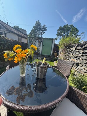 A round glass table with a metal bucket containing a bottle, surrounded by wicker chairs.