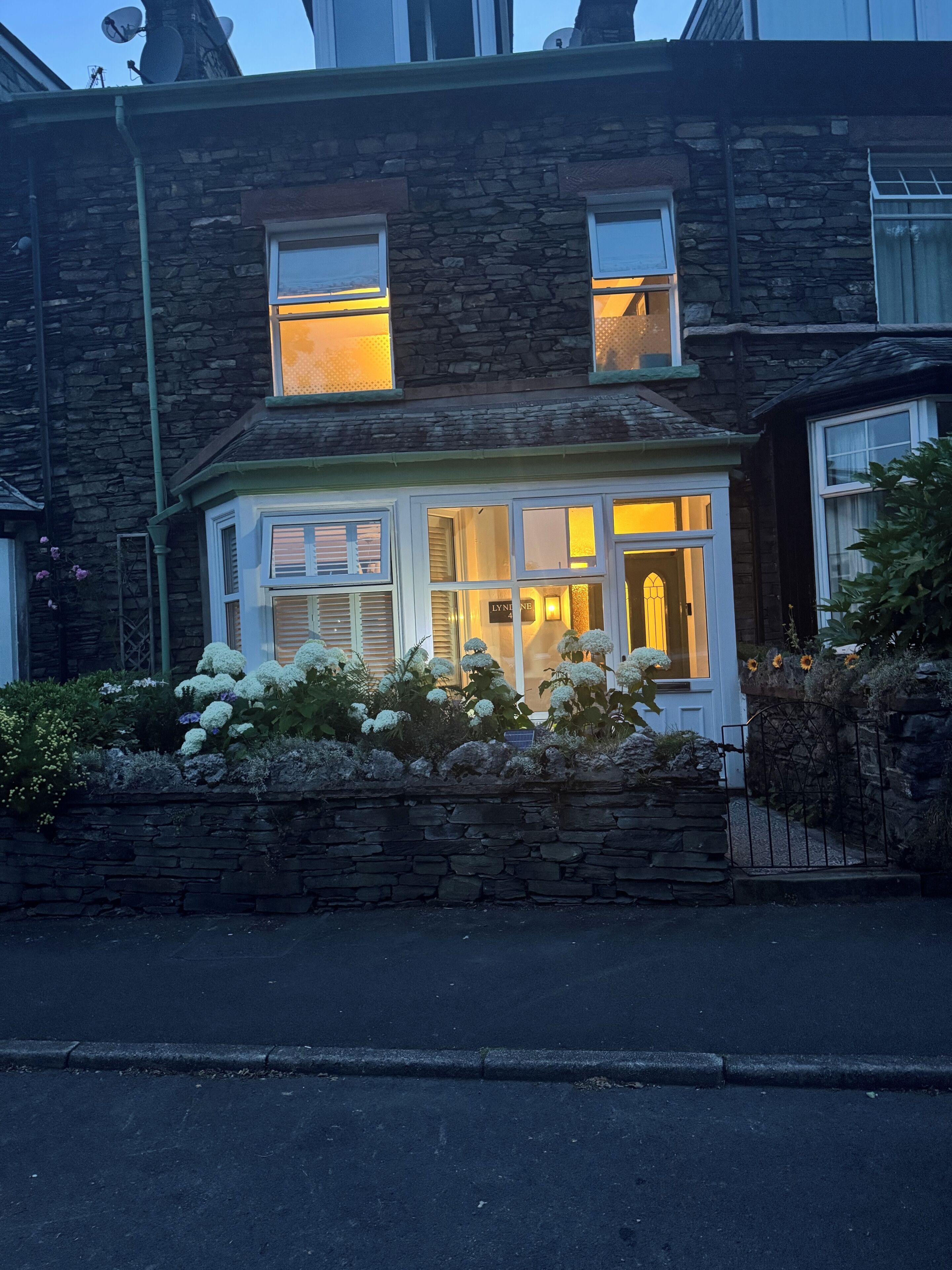 A stone house with a bay window, a visible door, and a stone wall in front.