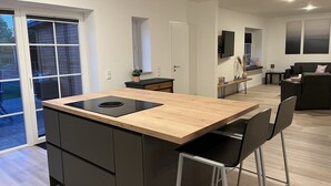 A modern kitchen with a large island, black cabinets, and a sliding glass door leading to a patio. - Vacation home "de Fofftein" in Bockhöft (Ellingstedt)