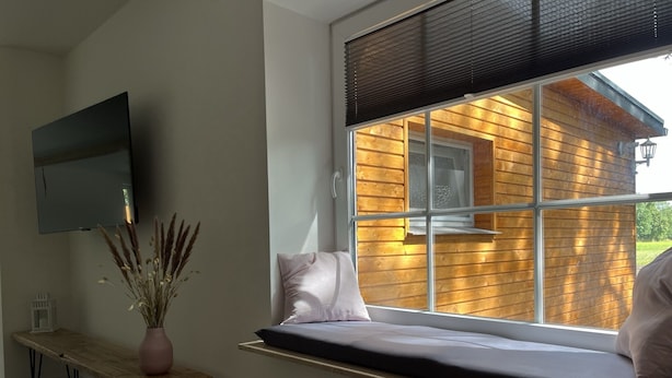 A room with a bed on a window seat, a flat-screen TV mounted on the wall, a wooden bench, and a vase with dried plants. - Vacation home "de Fofftein" in Bockhöft (Ellingstedt)