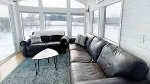 Un salon moderne avec un canapé d’angle, une petite table et de grandes fenêtres donnant sur un paysage enneigé.