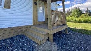 Une terrasse en bois avec un porche menant à une maison mobile blanche dotée d’une porte et d’une fenêtre.