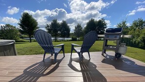 Une terrasse en bois avec deux fauteuils Adirondack donnant sur un barbecue et un lac.
