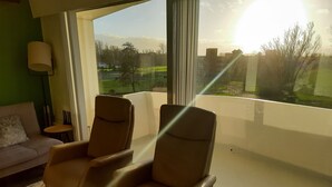 A room with two leather armchairs, a green sofa, and a large window offering a view of a green landscape and buildings.