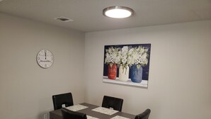 A dining area with a table and four chairs, a clock on the wall, and a painting of vases with flowers. - Home in NW Austin 2 BR 2 BA Private Parking Private Patio Pet Stays for Free ! (Austin)