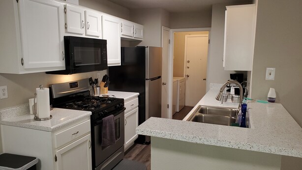 A compact kitchen with white cabinetry, a black stove, a microwave, and a refrigerator. - Home in NW Austin 2 BR 2 BA Private Parking Private Patio Pet Stays for Free ! (Austin)