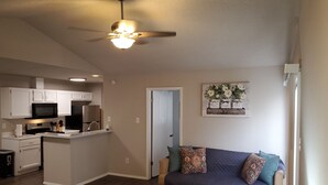A modern living room with a dark-colored sofa, a small table, and a ceiling fan. - Home in NW Austin 2 BR 2 BA Private Parking Private Patio Pet Stays for Free ! (Austin)