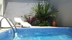 Piscina com borda azulejada, uma cadeira de praia branca e um vaso com planta.