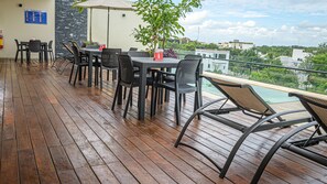 An outdoor patio with wooden flooring, black wicker furniture, and a view of a pool and buildings in the background. - Moonshine Tulum Hotel  (Tulum)