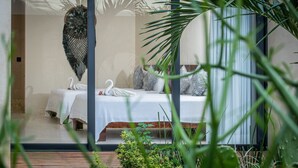A bedroom with two beds, each with a swan towel, a large decorative wall piece, and a view of a garden. - Moonshine Tulum Hotel  (Tulum)