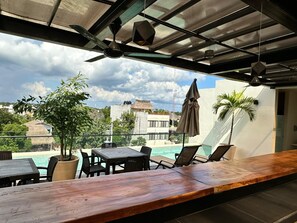 Terraza en la azotea con piscina, sillones de descanso y un bar de madera.