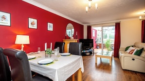 Ein Essbereich mit Tisch für vier Personen, einer Couch, einem Fernseher und einem Fenster mit Vorhängen.