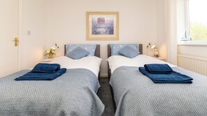 Ein Doppelzimmer mit zwei Betten, jeweils mit blauer Decke und Kissen, einem gerahmten Bild an der Wand und einem Fenster mit Blick.