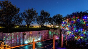 Eine Holzterrasse mit Seilbarriere, einem Baum und einem Zaun mit bunten Lichtern.