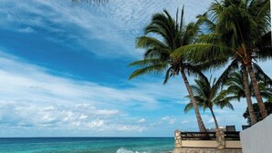 A beach with clear blue water, palm trees, and a stone wall. - Cozumel Penthouse Condo-Las Brisas 702 (San Miguel de Cozumel)