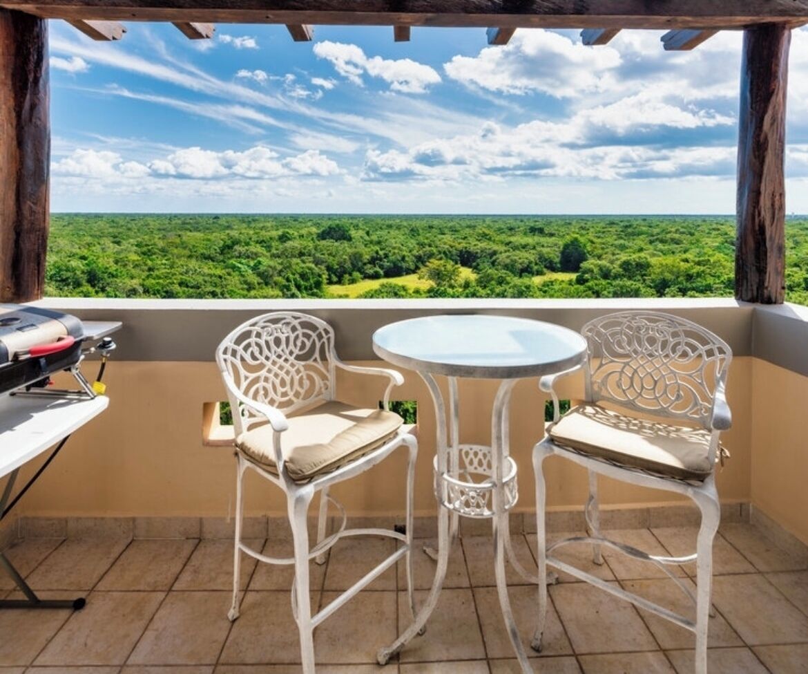 Une terrasse extérieure avec deux chaises en métal blanc et une petite table ronde, donnant sur un paysage verdoyant luxuriant.