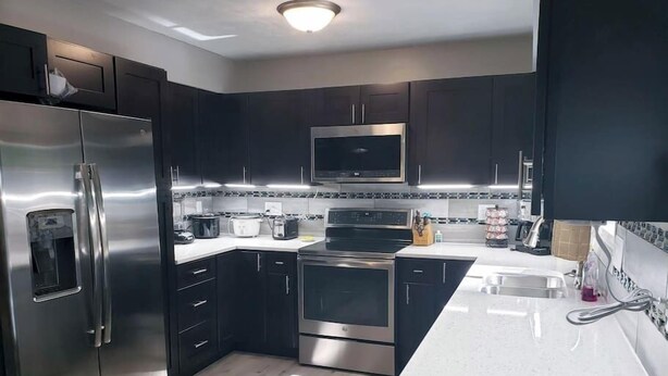 Une cuisine moderne avec des meubles de couleur sombre, des appareils en acier inoxydable, un four à micro-ondes, une cuisinière et un évier.