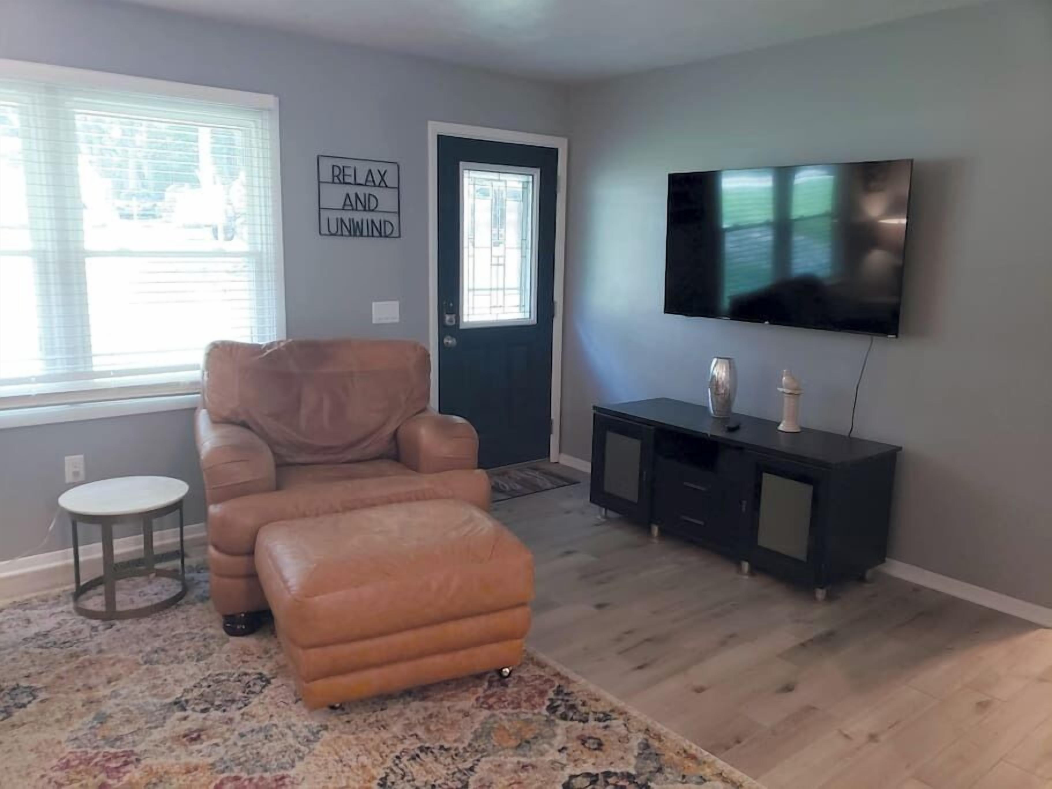 Un salon avec un fauteuil en cuir, un pouf et un téléviseur à écran plat posé sur un meuble noir.