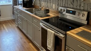 A modern kitchen with a stainless steel stove, a built-in oven, and a sink with a faucet. There are wooden cabinets and a window with curtains. - Newly renovated1 Bedroom 1 Bath in the Heart of Downtown Ellsworth.  (Ellsworth)