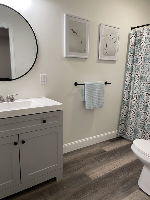 A bathroom with a white sink, gray cabinets, a round mirror, and a shower curtain with a floral pattern.