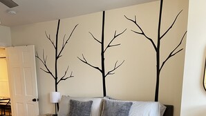 A bedroom with a large bed, a nightstand, a lamp, and a wall with tree decals. - Newly renovated1 Bedroom 1 Bath in the Heart of Downtown Ellsworth.  (Ellsworth)