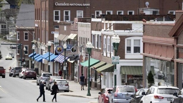A street view with a bank, shops, and parked cars.