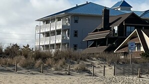 Un immeuble situé en bord de mer, avec plusieurs étages, une véranda et une enseigne indiquant qu’il se trouve près de la plage.