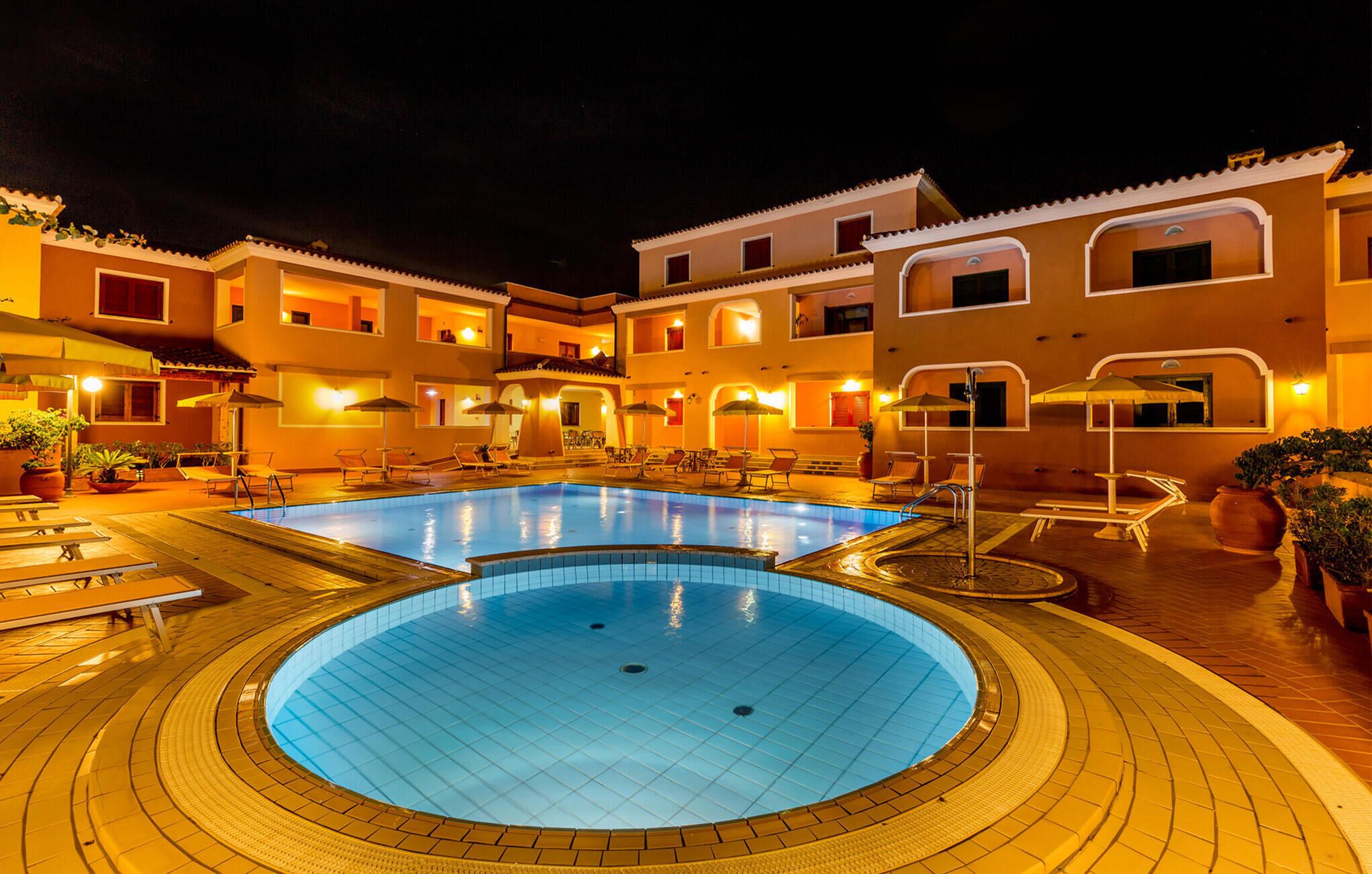 A swimming pool with lounge chairs and umbrellas, surrounded by a building with multiple balconies and windows.