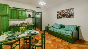 Una habitación con armarios de madera verde, una mesa de comedor con platos y vasos, un sofá verde con cojines estampados y un cuadro en la pared.