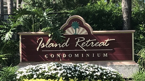A sign for Island Retreat Condominium surrounded by lush greenery and white flowers. -  FALL in love with this 1 BD/1 BA at Island Retreat. Plenty of dates available. (St. Simons Island)