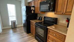 A kitchen with wooden cabinets, a black refrigerator, a microwave, and an oven. -  FALL in love with this 1 BD/1 BA at Island Retreat. Plenty of dates available. (St. Simons Island)