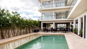 A modern building with a pool, outdoor seating, and a view of the sky. - OCEAN VIEW APARTMENT (Dzemul,)