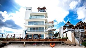 A multi-story hotel with a prominent 'BROWN' sign, a wooden deck with seating, and a beachside location. - OCEAN VIEW APARTMENT (Dzemul,)