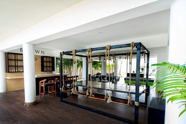 A spacious indoor area with a wooden floor, a seating area with tables and chairs, and a rope swing structure.