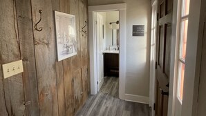 Ein Korridor mit Holzwänden, einem gerahmten Bild, einem Lichtschalter und einer Tür zu einem Badezimmer.