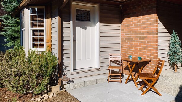Una casa con fachada de ladrillo, una puerta blanca y un pequeño patio con una mesa y sillas.