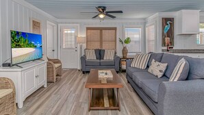 A living room with a television, two sofas, a coffee table, and a ceiling fan. - Peach Beach Retreat-Restored Rustic Gem- 3BR 1.5B (Murrells Inlet)