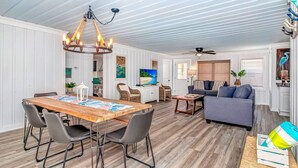 A spacious living area with a wooden dining table, gray chairs, a gray sofa, and a ceiling fan. - Peach Beach Retreat-Restored Rustic Gem- 3BR 1.5B (Murrells Inlet)