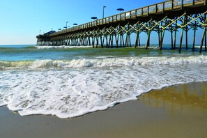Un molo che si protende verso l'oceano, con una spiaggia sabbiosa in primo piano.