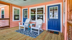 A porch with a wooden floor, two Adirondack chairs, and a blue door. - Peach Beach Retreat-Restored Rustic Gem- 3BR 1.5B (Murrells Inlet)