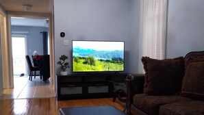 A living room with a flat-screen TV on a stand, a brown leather sofa, a black ottoman, and a small potted plant. - Detached 3 BR home in Ajax,ON (Ajax)