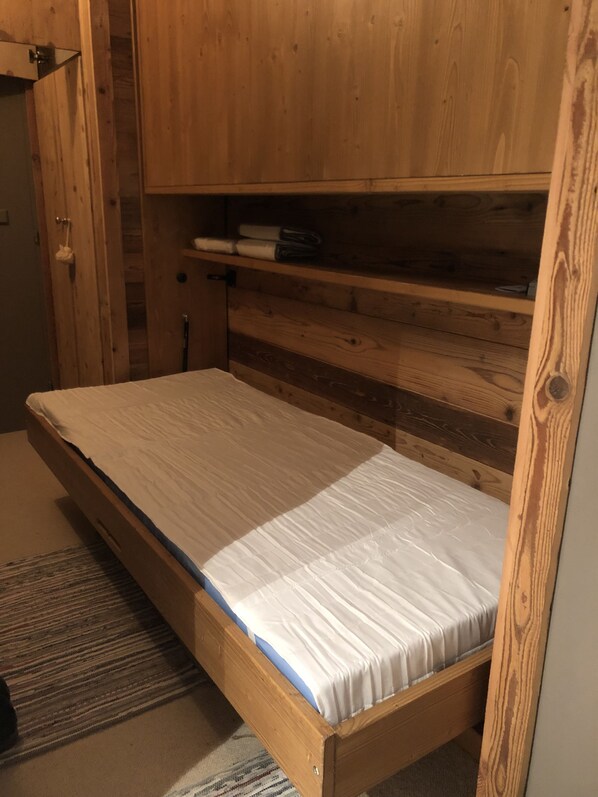 A wooden bed with a mattress, a wooden wardrobe, and a small shelf. - Tignes Val Claret: A Cozy Retreat at the Foot of the Slopes (Tignes Val Claret)
