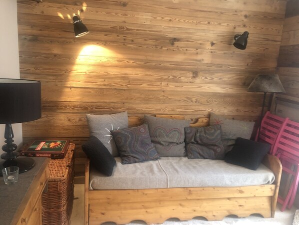 Tunnelmallinen huone, jossa on puuseinä, kuviollisilla tyynyillä varustettu sohva, lamppu ja Scrabble-lautapeli.