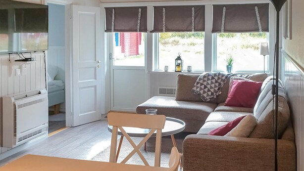 A cozy living area with a sofa, a small round table, and a chair. There is a door leading to another room, and windows with curtains. - Cozy home in Sysslebäck with kitchen (Sysslebäck)