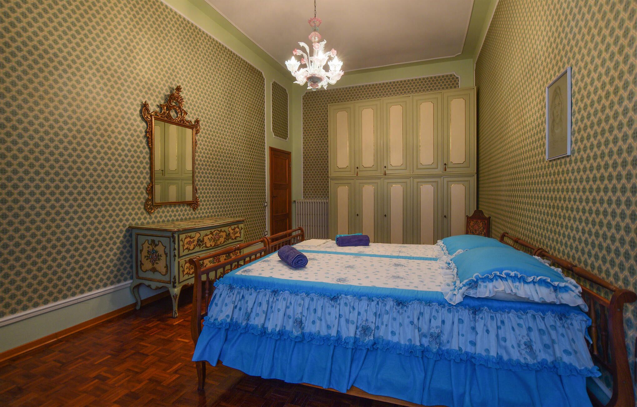 A bedroom with a wooden bed, a dresser, a mirror, and a chandelier.
